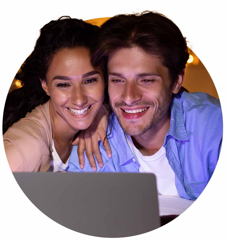 Two smiling people watching something on a laptop.